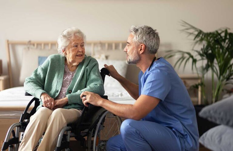Resident choosing clothing with a caregiver in a bright, private assisted living room.